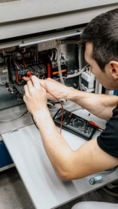 An electrician uses a multimeter to test and diagnose connections in an open electrical panel. 